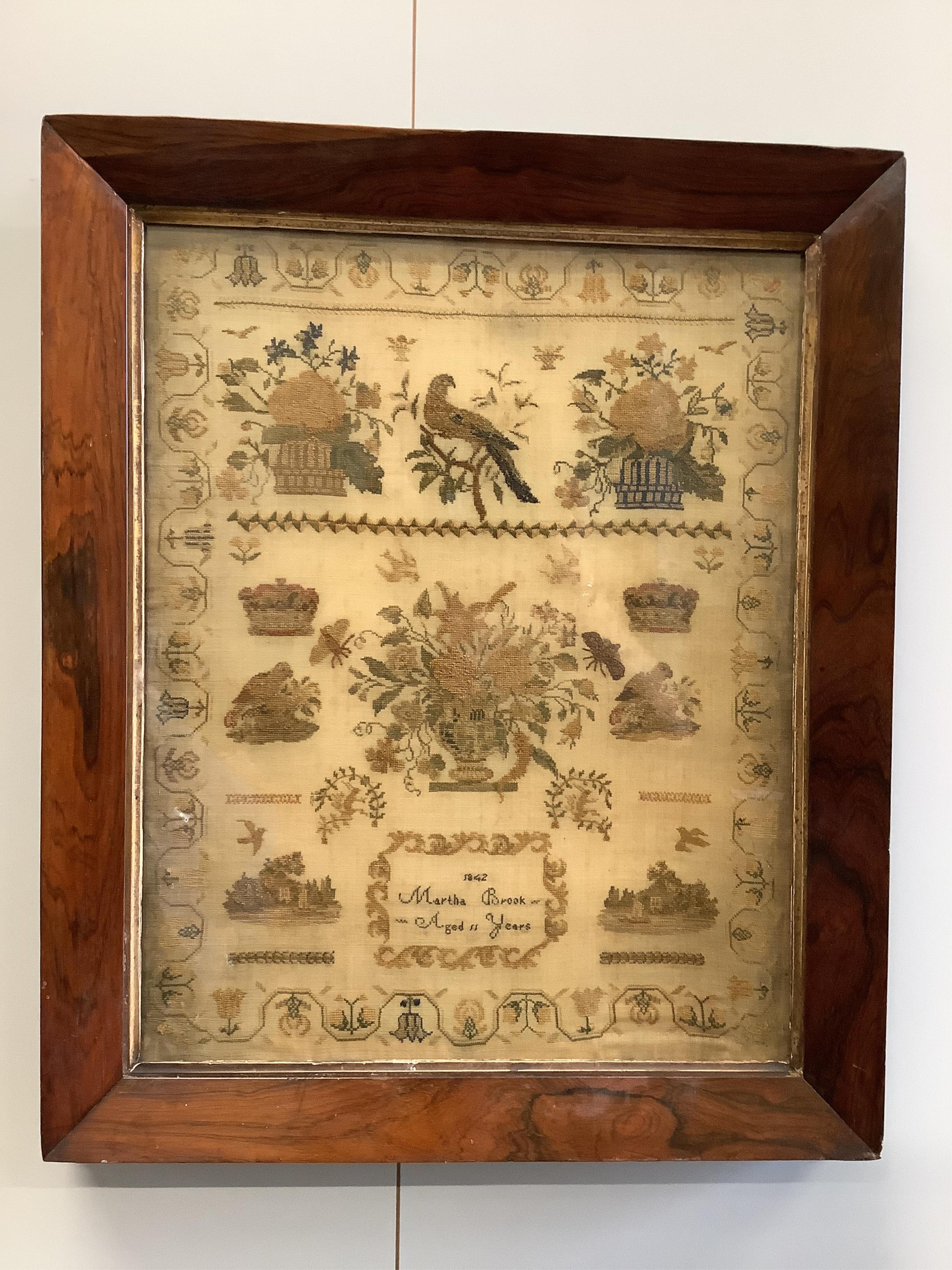 A rosewood framed sampler, dated 1842, by Martha Brook, aged 11years, worked above with large motifs of flower baskets and a bird, a vase of flowers beneath, surrounded by crowns, butterflies and chicks above two small c